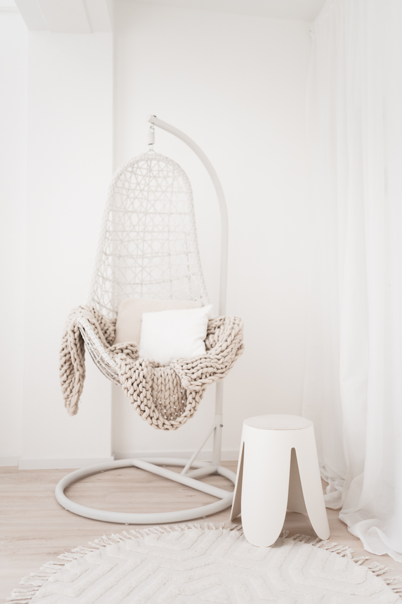 Hängesessel in weiß mit beiger Decke darauf.