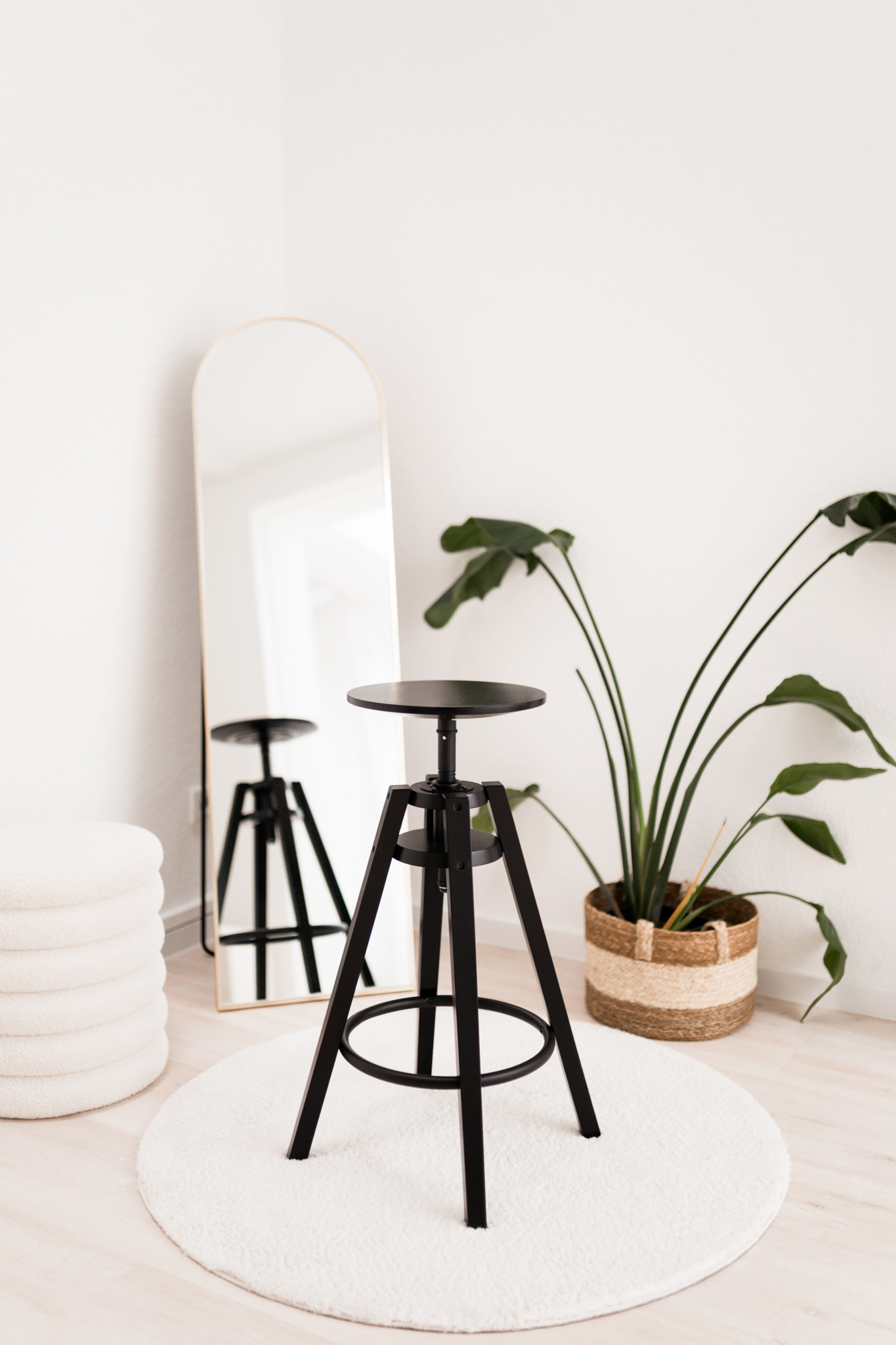 Schwarzer Hocker vor Spiegel mit Pflanze im Bild.