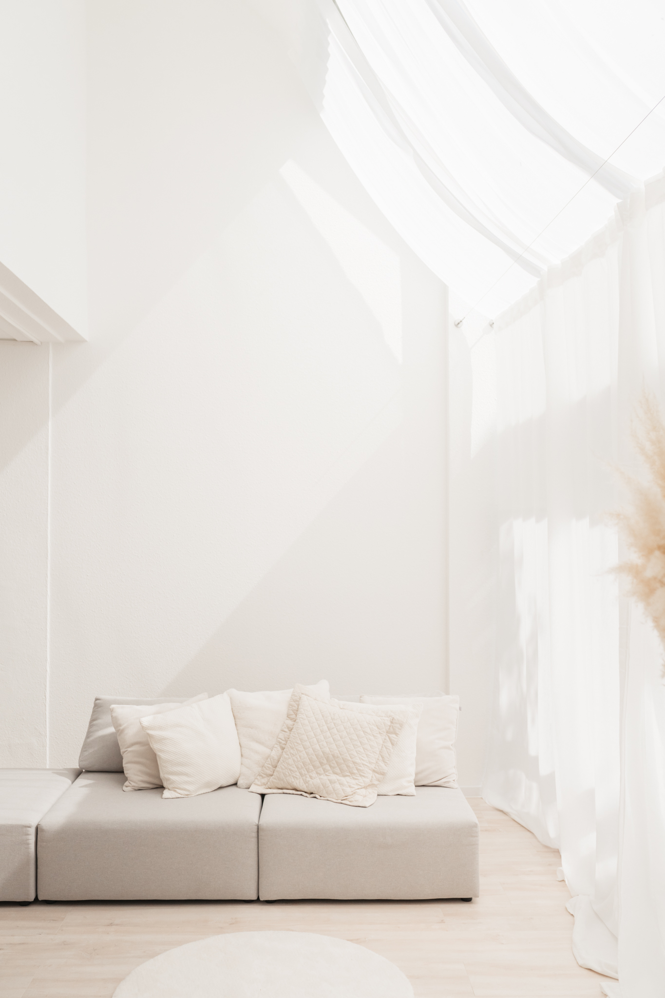 Blick ins Studio zum Sofa an der Wand und den weißen Vorhängen vor den großen Fenstern an der rechten Seite.